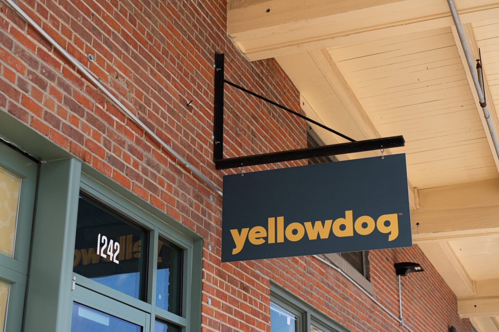 Hanging sign with the brand name "YellowDog" in yellow text on black, hanging from a brick wall.