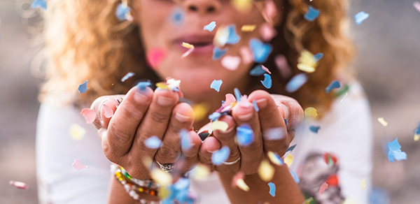 Close-up of a woman blowing hand-fulls of confetti toward the camera.