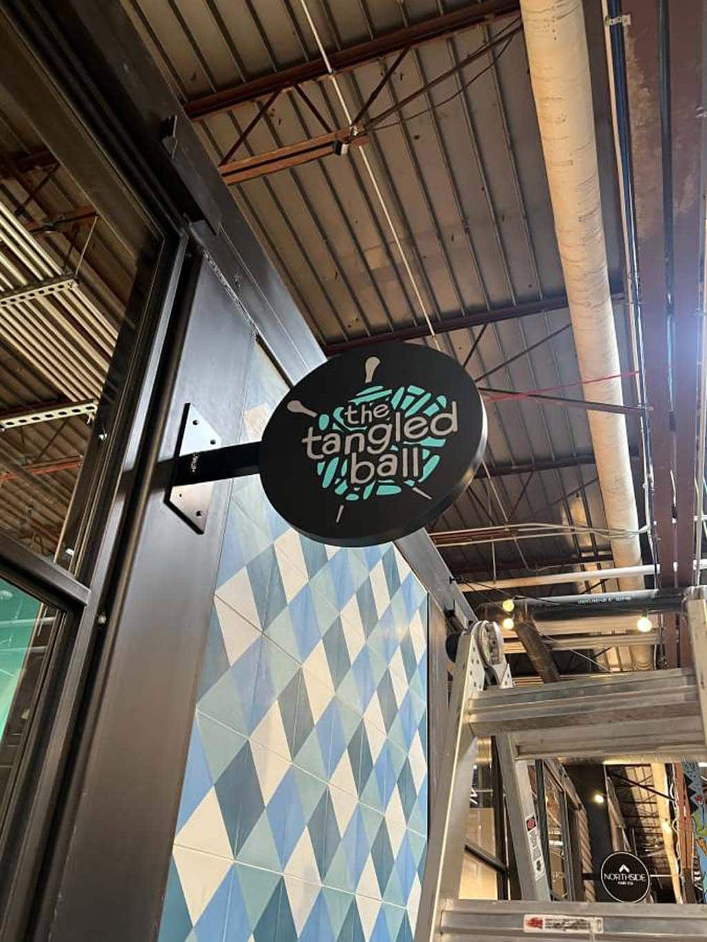 "the tangled ball" business name and logo on a circular, three-dimensional sign affixed to a wall.
